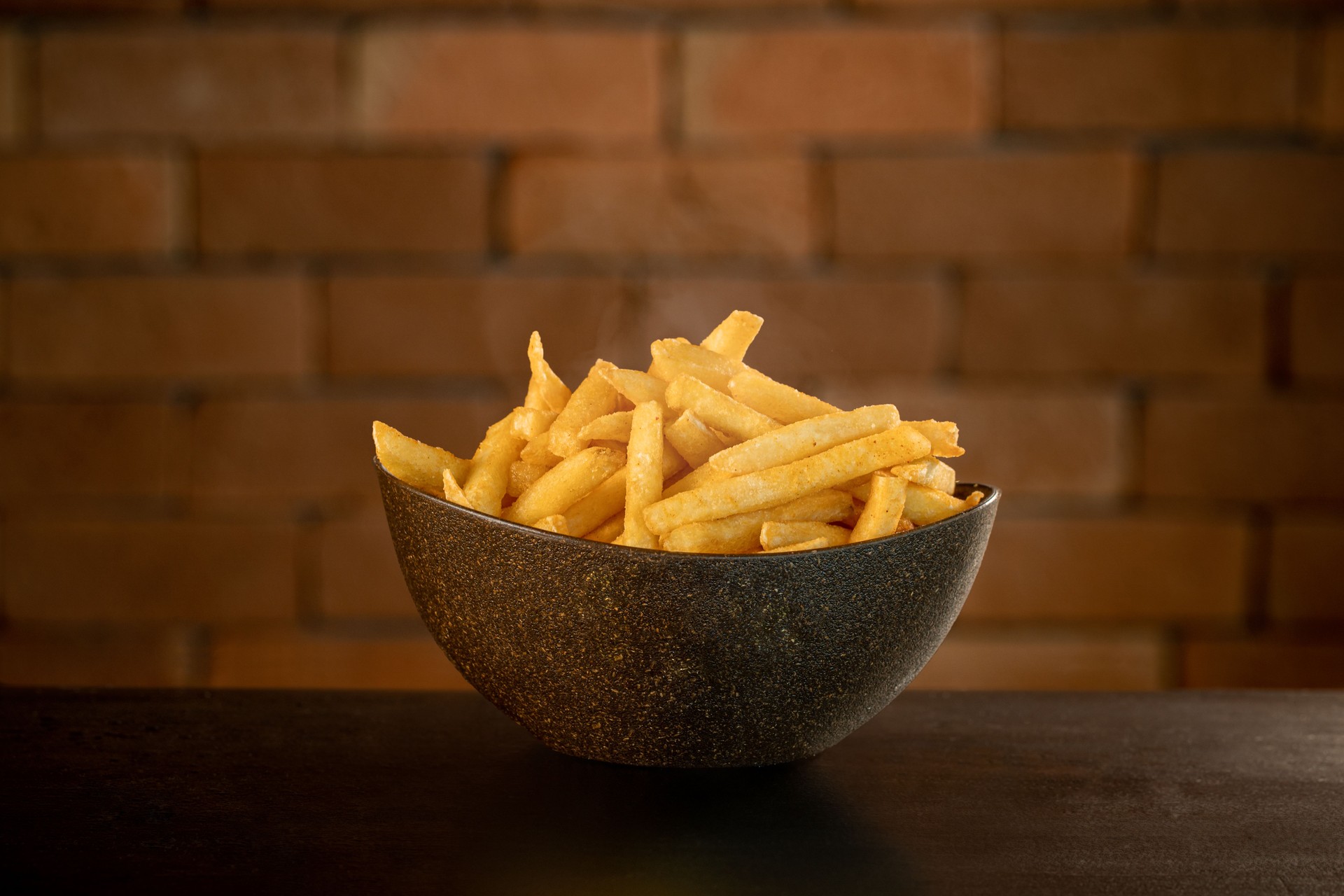 French fries in pot on table in front of brick wall